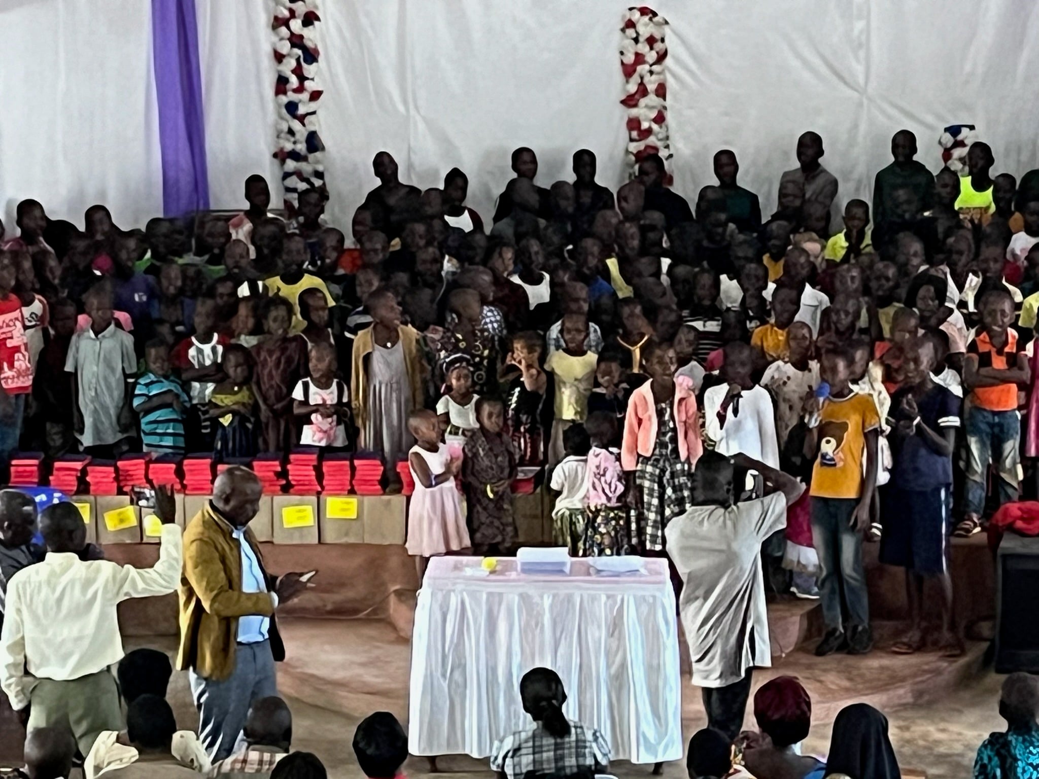 Children on stage beside workbook stacks, 2024.